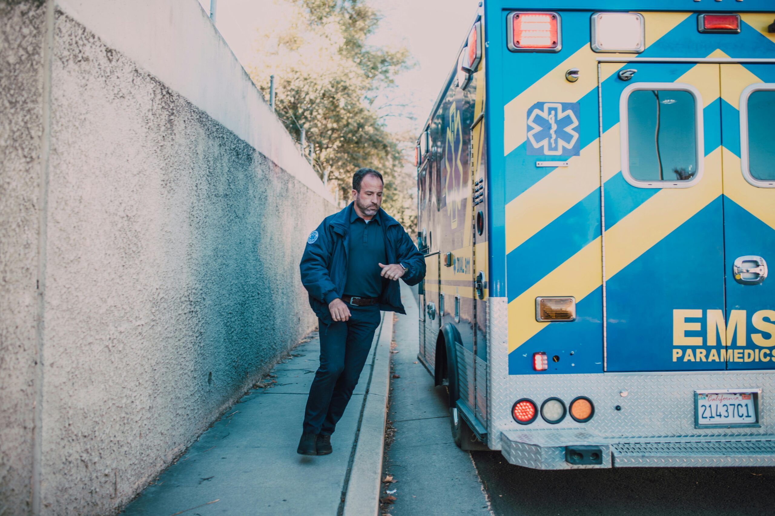 Emergency medical technician beside parked ambulance on roadside in daylight.